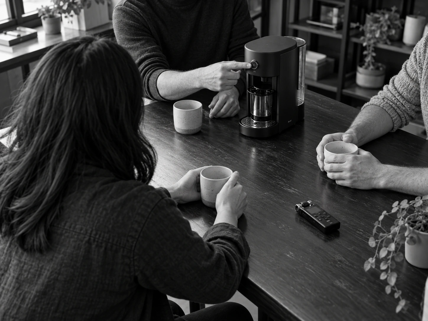 Black-and-white customer research scene: a small group discussing and testing a product, photographed from behind with no faces visible.